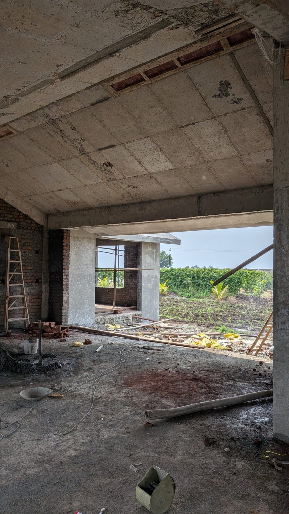 The living room shell under its sloping concrete roof, looking out to the fields, site photo