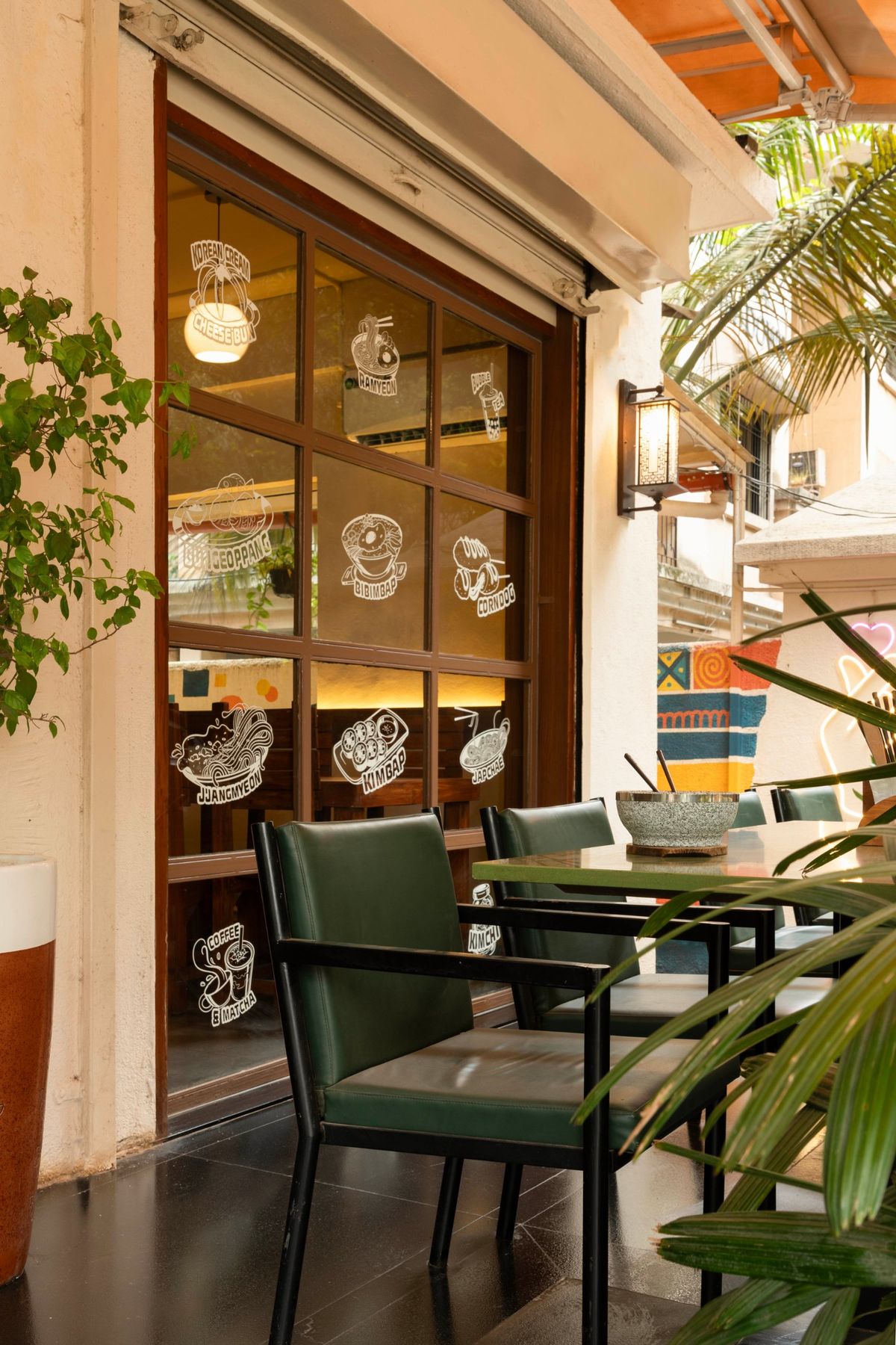 Glazed shopfront with illustrated menu decals and green chairs