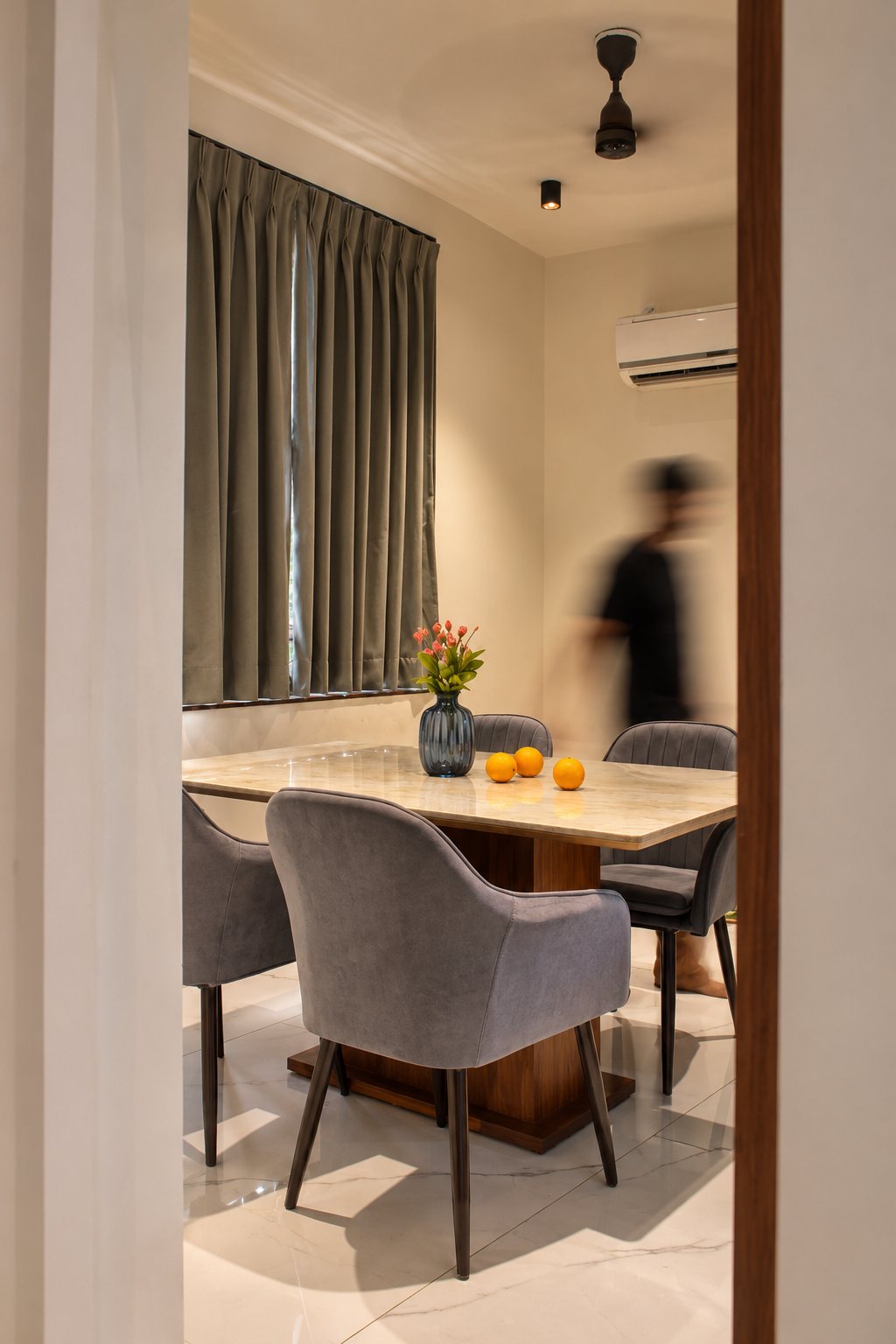 Dining room with a stone-topped table on a walnut pedestal and grey upholstered chairs, seen through a doorway, photo